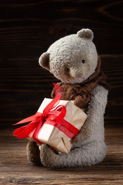 Photo vintage teddy bear holding gift box on wooden background