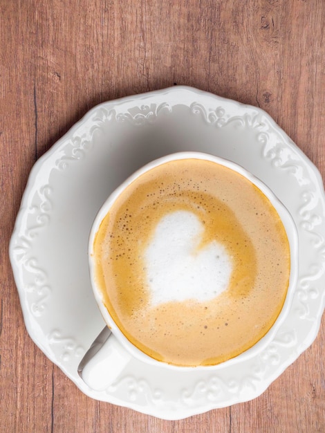 Vintage white coffee cup with heart shape latte art on wood table