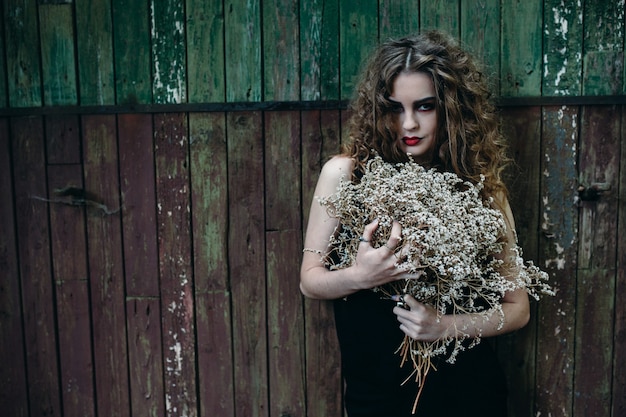 Vintage woman as witch, posing against the backdrop of an abandoned place on the eve of Halloween