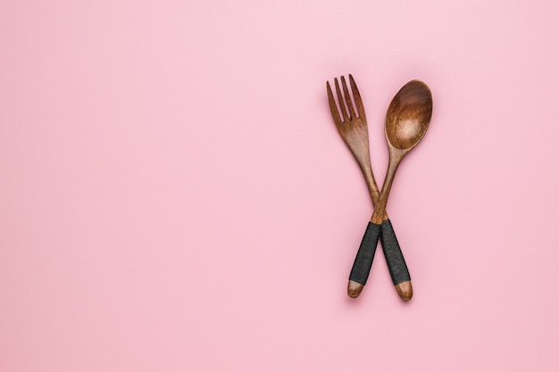 Photo vintage wooden spoon and fork on pink background. space for text.