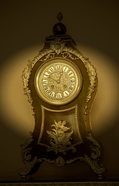 Photo vintage wooden table clock with nineteenth century golden elements in dark vignette