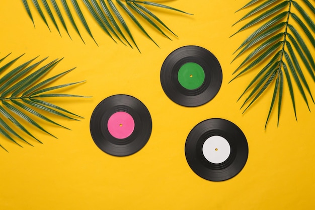 Vinyl records and palm green leaves on yellow background Music concept Tropical composition Top view Flat lay