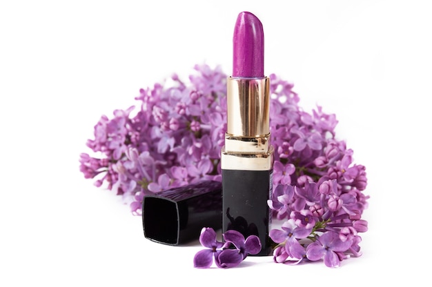 Violet lipstick and lilac flowers on white background