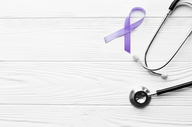 Photo violet ribbon and stethoscope on timber background