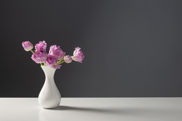 Violet tulips in white vase on background gray wall