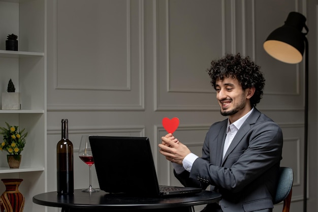 Virtual love handsome cute guy in suit with wine on a distance computer date holding red heart