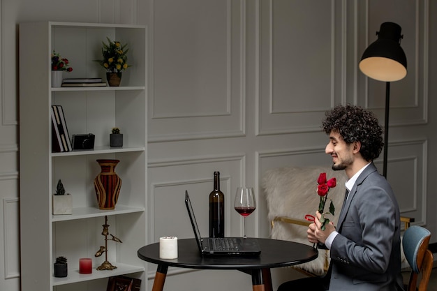 Virtual love handsome cute guy in suit with wine on a distance computer date holding roses