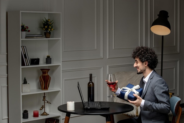 Virtual love handsome cute guy in suit with wine on a distance computer date holding wine and gift