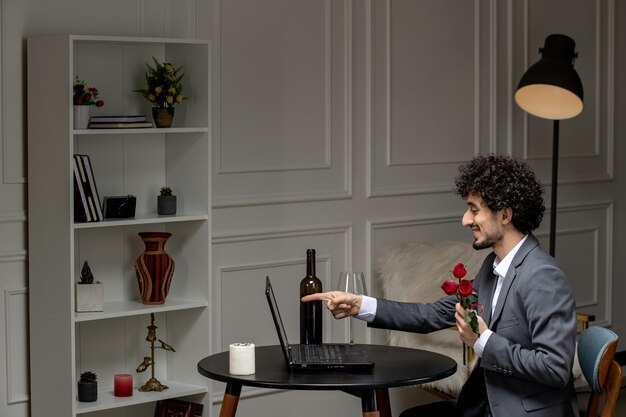 Virtual love handsome cute guy in suit with wine on a distance computer date pointing at screen