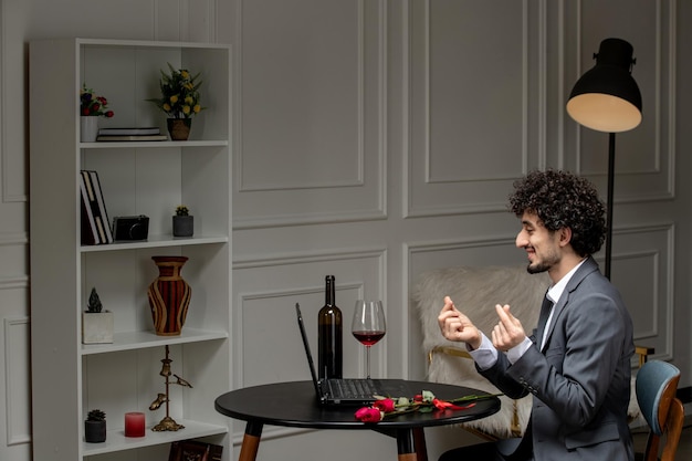 Virtual love handsome cute guy in suit with wine on a distance computer date showing finger hearts