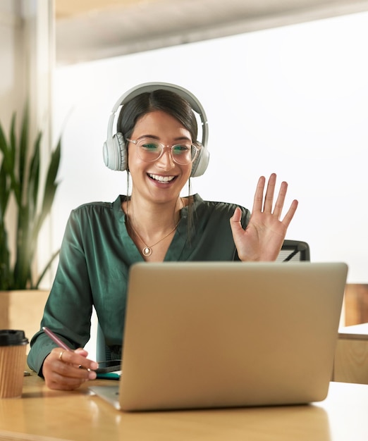 Virtual meeting business woman and wave on a video call with headphones and greeting Laptop working and female employee with webinar at a company with computer and digital communication at office