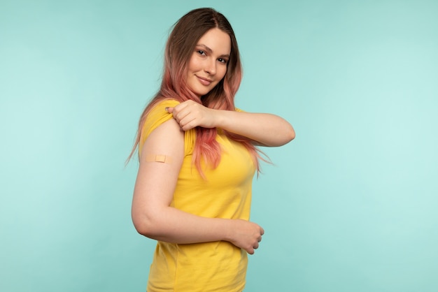 Photo virus protection. excited vaccinated woman showing arm after injection, holding shirt sleeve and smiling to camera over studio background with empty space. coronavirus, covid-19 vaccine concept.