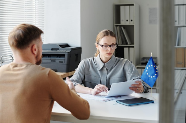 Visa service specialist sitting at table in front of man looking through documents checking data dur