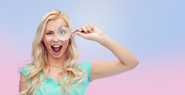 vision, exploration, investigation, education and people concept - happy smiling young woman or teenage girl looking through magnifying glass over rose quartz and serenity gradient background