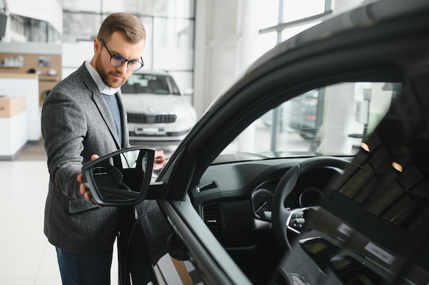 Visiting car dealership Handsome bearded man is stroking his new car and smiling