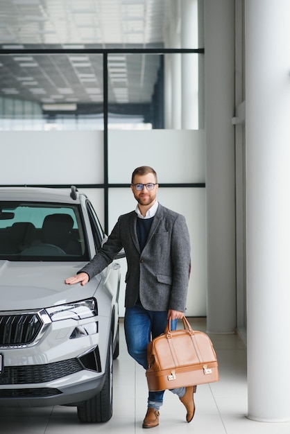 Visiting car dealership Handsome bearded man is stroking his new car and smiling