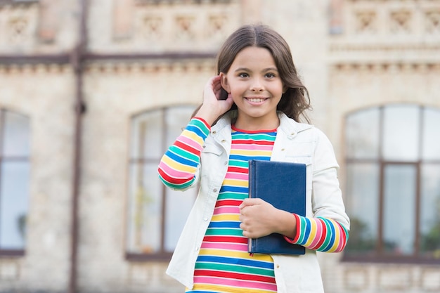 Visiting library can encourage reading and exploration in children Interesting story for kid Homework concept Little girl hold book Small girl with book urban background Book from library