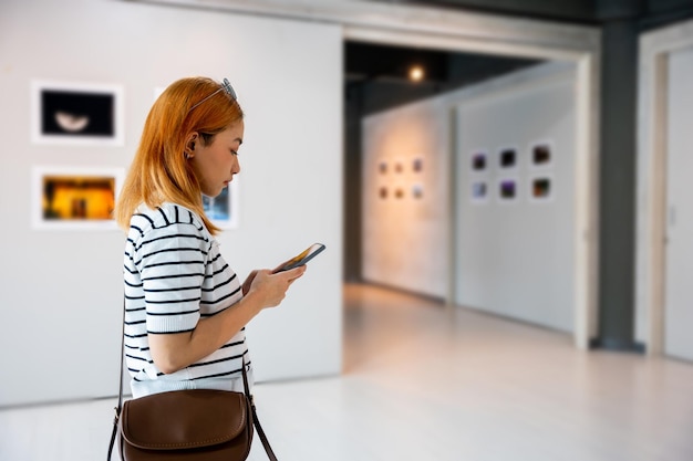 Visitor woman standing takes picture art gallery collection in front framed paintings pictures