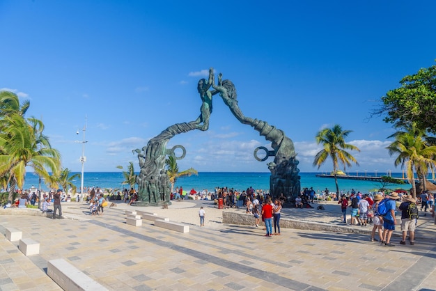 Visitors mingling on Fundadores Park beach at Playa del Carmen on the Caribbean coast of Riviera Maya with performers under the Portal Maya sculpture