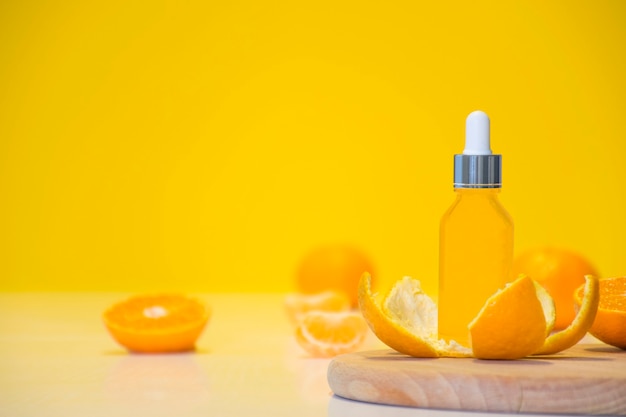 Vitamin C serum cosmetic bottle in tangerine peel with orange pieces on yellow background with copy space.