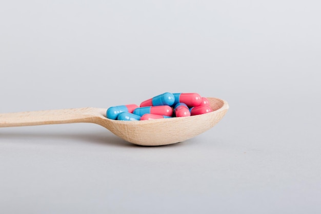 Vitamin capsules in a spoon on a colored background Pills served as a healthy meal Red soft gel vitamin supplement capsules on spoon