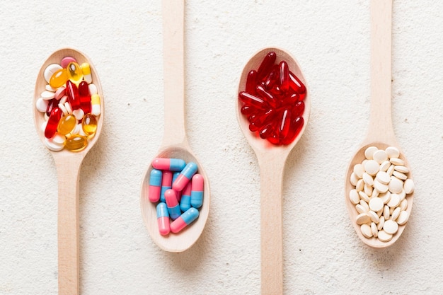 Vitamin capsules in a spoon on a colored background Pills served as a healthy meal Red soft gel vitamin supplement capsules on spoon