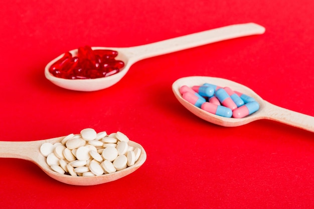 Vitamin capsules in a spoon on a colored background Pills served as a healthy meal Red soft gel vitamin supplement capsules on spoon