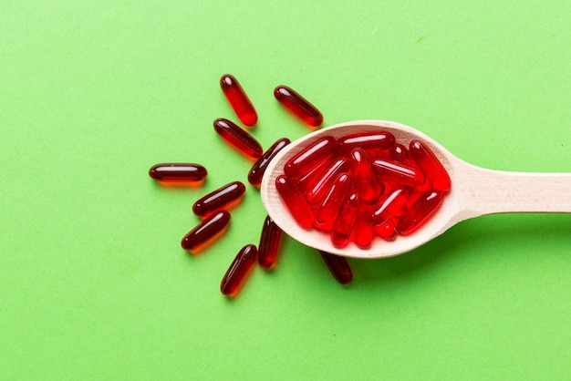 Vitamin capsules in a spoon on a colored background Pills served as a healthy meal Red soft gel vitamin supplement capsules on spoon