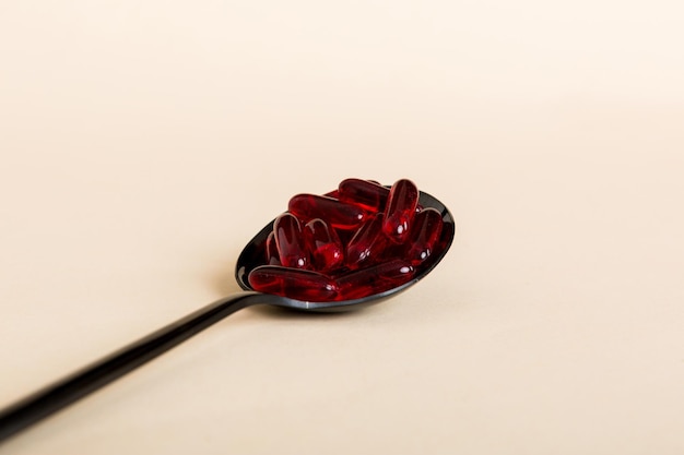 Vitamin capsules in a spoon on a colored background Pills served as a healthy meal Red soft gel vitamin supplement capsules on spoon