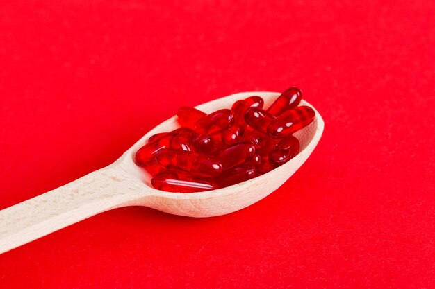 Vitamin capsules in a spoon on a colored background Pills served as a healthy meal Red soft gel vitamin supplement capsules on spoon