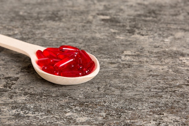 Vitamin capsules in a spoon on a colored background Pills served as a healthy meal Red soft gel vitamin supplement capsules on spoon