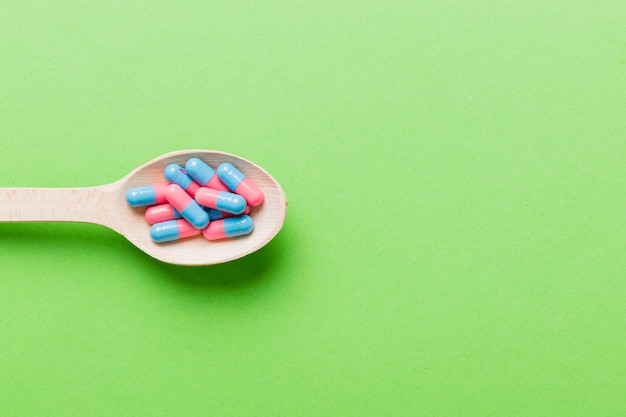 Vitamin capsules in a spoon on a colored background Pills served as a healthy meal Red soft gel vitamin supplement capsules on spoon