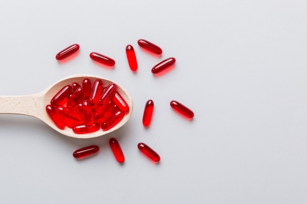 Vitamin capsules in a spoon on a colored background Pills served as a healthy meal Red soft gel vitamin supplement capsules on spoon