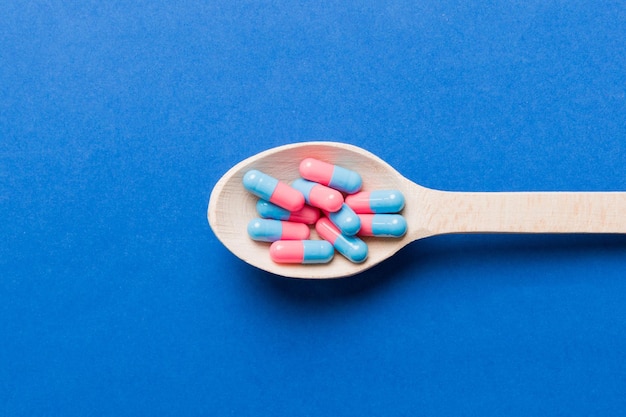 Vitamin capsules in a spoon on a colored background Pills served as a healthy meal Red soft gel vitamin supplement capsules on spoon