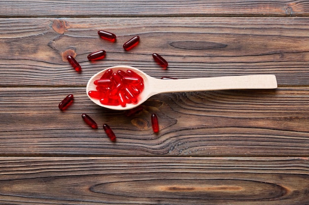 Vitamin capsules in a spoon on a colored background Pills served as a healthy meal Red soft gel vitamin supplement capsules on spoon