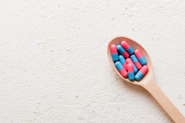 Vitamin capsules in a spoon on a colored background Pills served as a healthy meal Red soft gel vitamin supplement capsules on spoon