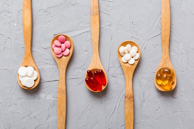 Vitamin capsules in a spoon on a colored background Pills served as a healthy meal Red soft gel vitamin supplement capsules on spoon