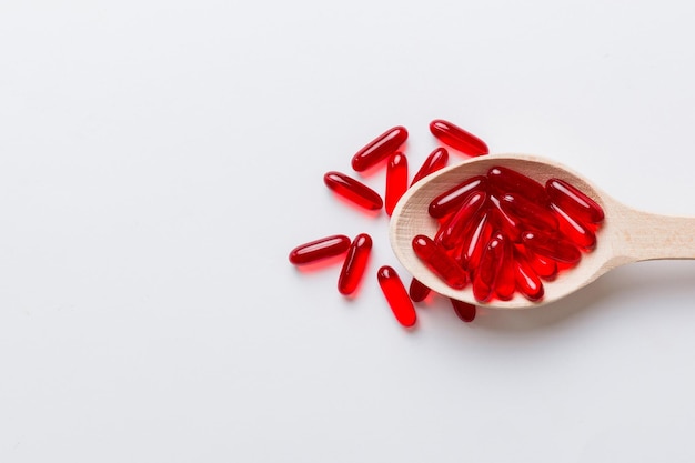 Vitamin capsules in a spoon on a colored background Pills served as a healthy meal Red soft gel vitamin supplement capsules on spoon