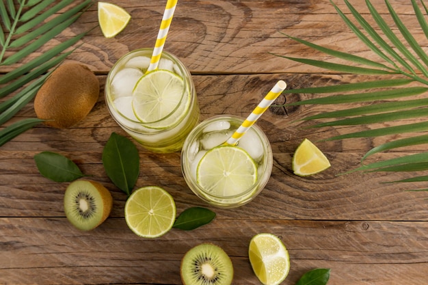 Vitamin water with kiwi and lime in modern glasses in the form of a beer can against the background of a wooden table fruits and tropical leaves