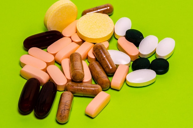 Vitamins in capsules and tablets on a green background.