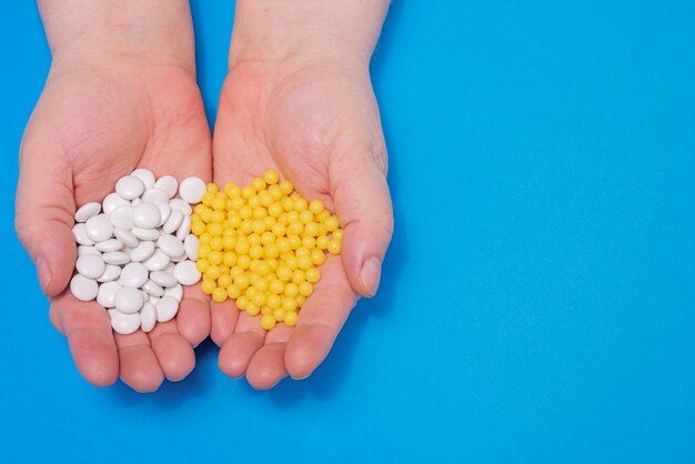 Vitamins in the hands of an adult white tablets and yellow capsules on a blue background, central v