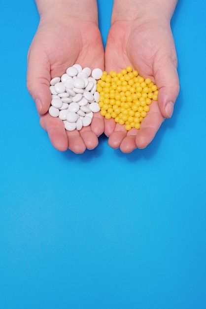 Vitamins in the hands of an adult white tablets and yellow capsules on a blue background, central v