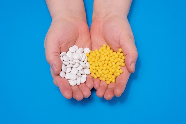 Vitamins in the hands of an adult white tablets and yellow capsules on a blue background