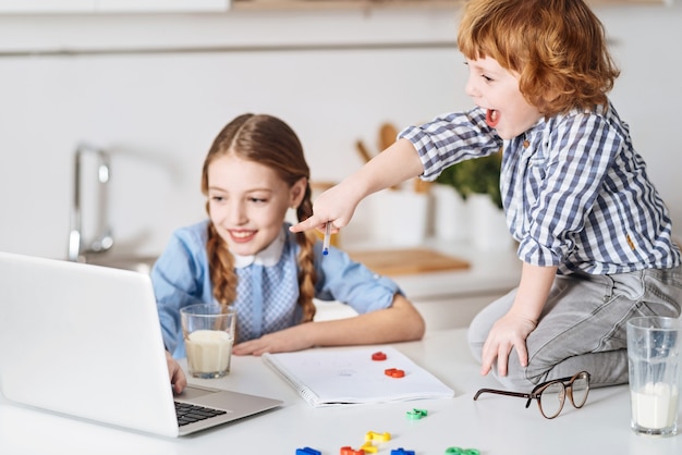 Vivid examples. Amusing nice energetic siblings watching some helpful videos on the laptop while learning new math formulas and enjoying their time together