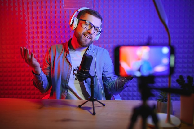 Vlogger using smartphone to film podcast in studio blogger with mobile phone microphone and headphones filming video for social media broadcasting career