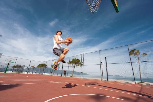 Vlore ALBANIA MAY 20 2022 Male basketball player shooting a jump shot outdoors Playing ball alone Sunrise ocean background