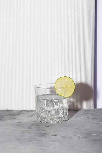 Vodka with ice and lime in glass on white background. Shadows and sunlight trendy