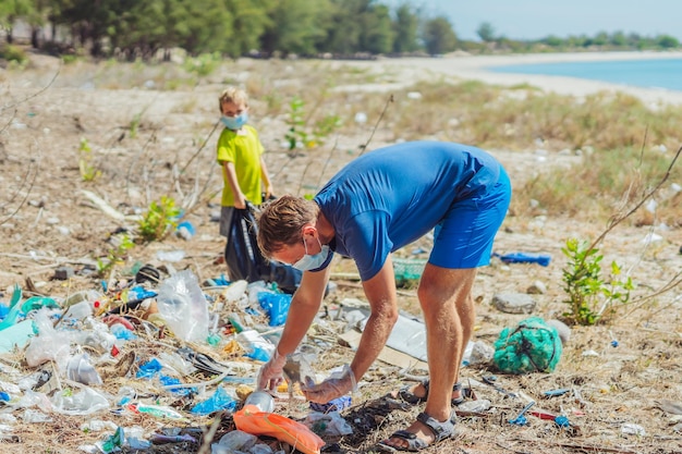 Volunteer blue face mask forest sand beach Son helps father hold black bag for pick up garbage Problem spilled rubbish trash planet pollution environmental protection Natural children education