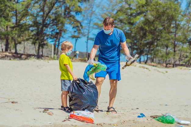 Volunteer blue face mask forest sand beach Son helps father hold black bag for pick up garbage Problem spilled rubbish trash planet pollution environmental protection Natural children education