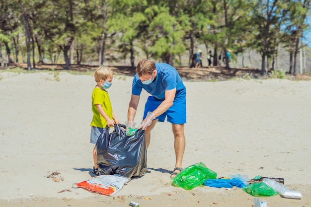 Volunteer blue face mask forest sand beach Son helps father hold black bag for pick up garbage Problem spilled rubbish trash planet pollution environmental protection Natural children education